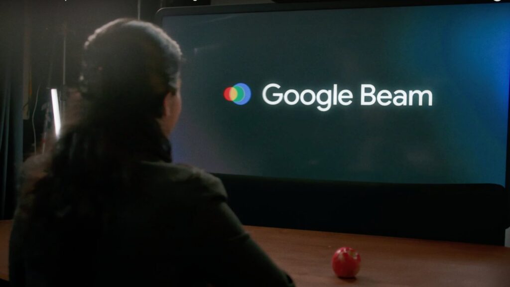 Woman sits in front of Google Beam screen displaying the logo